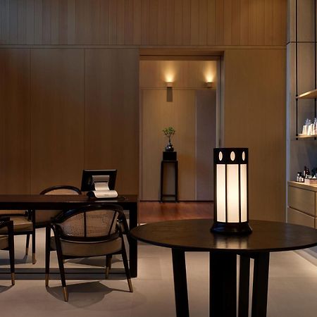 더 루마 호텔 앤 레지던스 쿠알라룸푸르 외부 사진 The photo shows a modern, minimalist interior space. It features a wooden wall with soft lighting, enhancing a calm atmosphere. In the foreground, there is a round table with a uniquely designed lamp on it. Surrounding the table, there are stylish wo