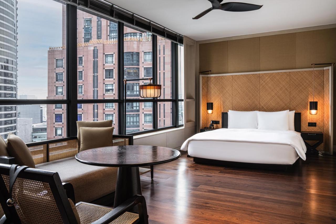더 루마 호텔 앤 레지던스 쿠알라룸푸르 외부 사진 The photo shows a modern hotel room featuring a large bed with white linens, situated against a backdrop of large windows that allow for ample natural light. The room includes a wooden floor and has a minimalist aesthetic, with a round table and two 