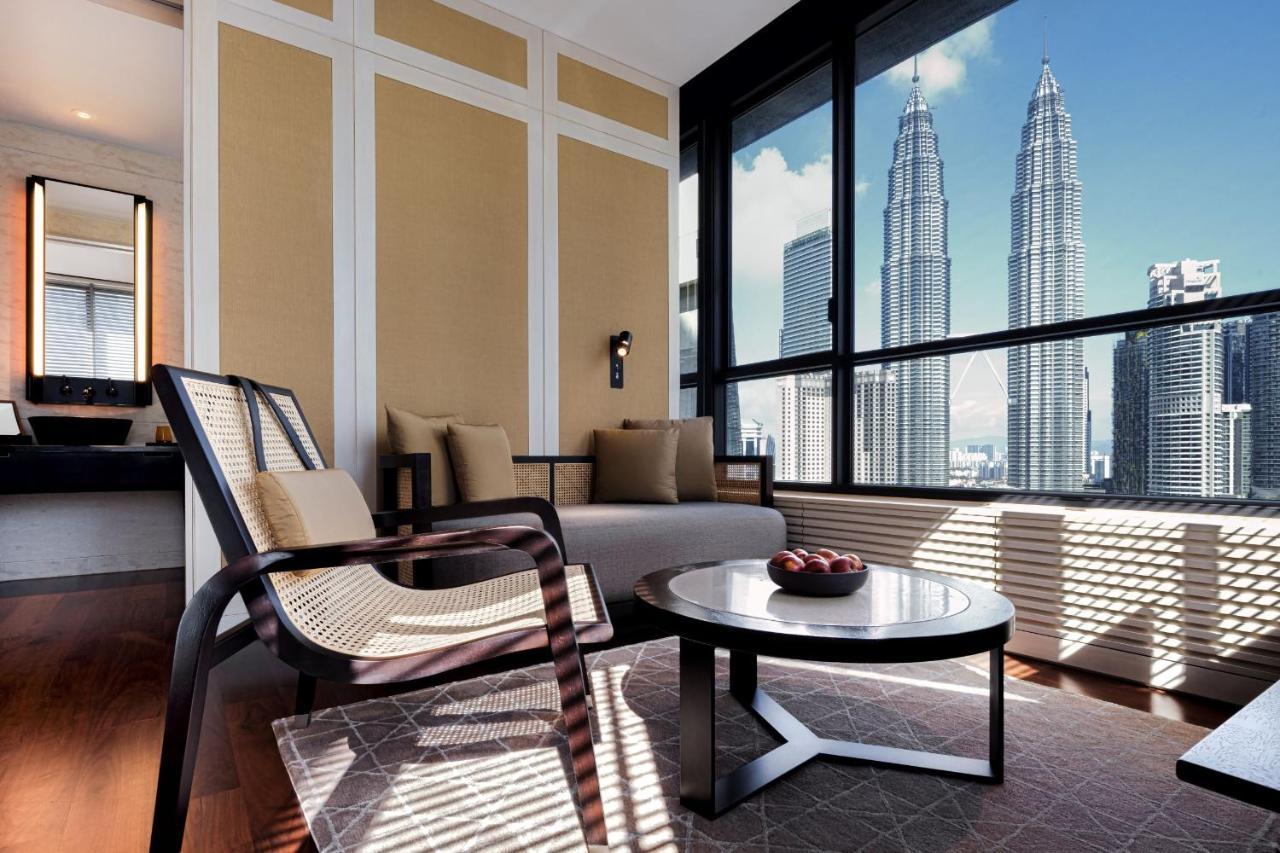 더 루마 호텔 앤 레지던스 쿠알라룸푸르 외부 사진 The photo depicts a stylish and modern interior of a living space, featuring a seating area with a comfortable chair and a sofa. There's a round coffee table in the center, adorned with decorative items. The room has large windows that offer an impre